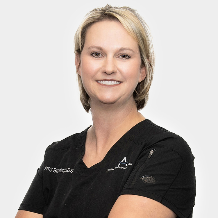 Dr. Amy Brewton-img Professional headshot of female dentist in black scrubs against white background, smiling at camera.